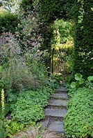 Informal pathway with stepping stones leading to decorative metal gate in archway through hedge. Garden: Rustling End Cottage, Hertfordshire. Owners: Mr and Mrs Wise