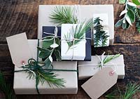 Lots of presents wrapped with brown and white paper and fastened with string, with gift tags and string.  Decorated with fir tree, yew tree and silvery foliage.