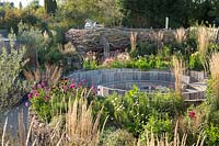 View over mixed borders of pub garden with willow fence and wooden seating. Jo Thompson garden Design, Ticehurst, East Sussex
