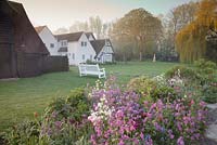 Spring bed with Tulipa with decorative white seat overlooking formal lawn mature trees and house. Garden: Ulting Wick, Essex. Owner: Philippa Burrough