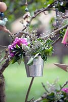 Little bucket with flowers hanging on branch.