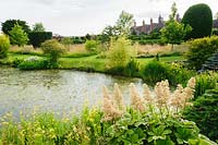 Garden pond fringed with rodgerias, primulas and bamboos, with house beyond. Felley Priory, Underwood, Notts, UK