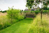 Paths are mown between long meadow grasses, here giving access to a wooden bench.  Felley Priory, Underwood, Notts, UK