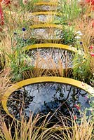 Pools of water surrounded by Anemanthele lessoniana, Echinops ritro and Salvia 'Hot Lips' - Kinetica, RHS Hampton Court Palace Flower Show 2017