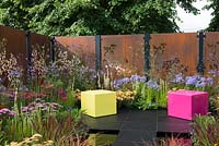 Decorative rusted steel panels enclose a colourful garden with pink and lime green cubed seating, plants include Agapanthus 'Blue Triumphator', Verbena bonariensis, Achillea 'Pretty Belinda', Achillea 'New Vintage Red' and Imperata cylindrica 'Rubra'- Colour Box, RHS Hampton Court Palace Flower Show 2017