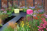 Colour Box garden. Rusty metal fence panels with laser cut floral patterns with red, pink and blue planted borders. Designers: Charlie Bloom and Simon Webster. RHS Hampton Court Palace Flower Show 2017