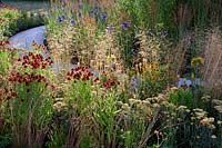 The Perennial Sanctuary Garden. Reds and Yellows in Spiralling borders. Helenium, Achillea, Kniphofia and grasses. Designer: Tom Massey. RHS Hampton Court Palace Flower Show 2017

