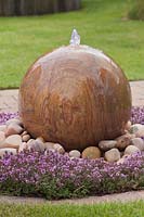 Rainbow stone sphere water feature surrounded by pebbles and Thymus plants - June, Summerfield Place, Cheshire