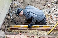 Builder using spirit level to square bricks for steps in a small London Garden