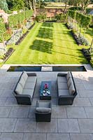 An elevated view of the newly contemporary English garden in Cheshire, designed by Louise Harrison-Holland and photographed in August. The patio area, with garden furniture and rill lead into a lawned walled garden, with plants including pleached Pyrus calleryana 'Chanticleer', Japanese anemones, Stachys, Persicaria, Ophiopogon planiscapus 'Nigrescens' and Miscanthus sinensis 'Kleine Fontaine'.