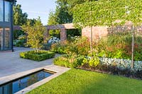 Long herbaceous borders along an old garden wall lead to a patio area and rill, designed by Louise Harrison-Holland. Plants include box hedging, Amelanchier lamarckii, pleached Pyrus calleryana 'Chanticleer', Japanese anemones, Stachys, Persicaria, Ophiopogon planiscapus 'Nigrescens' and Miscanthus sinensis 'Kleine Fontaine'
