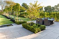 Long herbaceous borders lead to a patio area with a rill and seating, designed by Louise Harrison-Holland. Plants include Amelanchier lamarckii, box hedging, pleached Pyrus calleryana 'Chanticleer', Japanese anemones, Stachys, Persicaria, Ophiopogon planiscapus 'Nigrescens', and Miscanthus sinensis 'Kleine Fontaine'