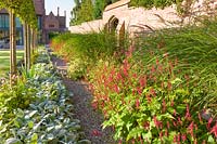 Long herbaceous borders along an old garden wall with gateway, designed by Louise Harrison-Holland. Plants include pleached Pyrus calleryana 'Chanticleer', Japanese anemones, Stachys, Persicaria, Ophiopogon planiscapus 'Nigrescens' and Miscanthus sinensis 'Kleine Fontaine'.