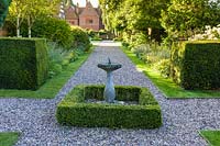 A sundial provides a focal point on a gravel path, midway along the 46 metre double herbaceous borders renovated as part of a project to create a modern garden at a large Cheshire garden. Design was by Louise Harrison-Holland. Planting includes clipped yew and box hedging.