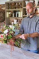 Man tying a bouquet with Dahlias, Rosa, Digitalis and foliage