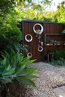 A rusty corten steel gate with a group of hand made white painted circular metal pots planted out with succulents. Pots include an Agave attenuata, Century plant and bamboo.