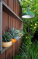 Collection of glazed pots planted with succulents and a green and white enamel outdoor light.