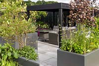 Small Garden with grey metal raised bed on wheels with herbs and flowers surrounding seating area. The Moveable Feast Garden - RHS Chatsworth Flower Show 2017 - Designer: Tanya Batkin