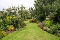 Curved lawn leading through mixed herbaceous border with trees