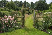 View through Rose arch to meadow garden with mown grass path in Summer