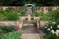 The herb garden in walled kitchen garden with focal point Armillary Sphere by David Harber. Raised beds with herbs including Rosemary, Monarda, Mint and Chives, made of drystone walls surrounded by Lavandula 'Imperial Gem'.   Steel arches with Sweet Peas and Flower beds with Lilies and Alchemilla mollis. Decorative chimney pots.