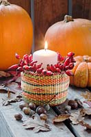 Candle and rosehips in a small basket, with autumn leaves, pumpkin, and acorns