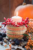 Candle and rosehips in a small basket, with autumn leaves, blackberries, pumpkin, and acorns