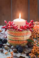 Candle and rosehips in a small basket, with autumn leaves, blackberries, pumpkin and acorns