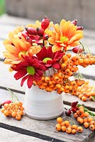 Autumnal display with Chrysanthemums in reds, yellows and oranges, rosehips and orange Pyracantha berries.