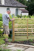 Man using spirit level to ensure post and fencing panel is straight