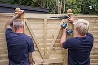 Men fixing gate in gap between fence panels