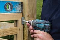 Details of man using spirit level while fixing fence panel to bracket
