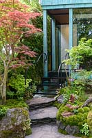Steps and balck banister leading to pavillion surrounded by Acers and moss planting  - Japanese Water Garden. Gosho No Niwa No Wall, No War. RHS Chelsea Flower Show 2017 