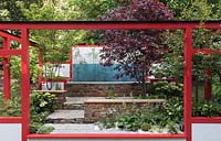 The Hagakure Hidden Leaves garden, red painted wooden frame, stone steps and seating area, glass panel screens with bamboo plants, planting of Acer palmatum 'Fireglow', Hosta venusta variegata, Hosta fortunei 'Whirlwind' and Hydrangea Heuchera sanguinea 'Alba' -RHS Chelsea Flower Show 2017