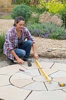 Woman using mallet to level paving slabs, checking using a spirit level