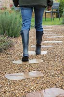 Woman in wellington boots walking on stepping stones through gravel garden