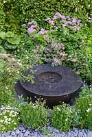 Round water feature made of black basalt concrete amongst planting of Rosa glauca, Rosa sericea subsp. omeiensis f. pteracantha, Chaerophyllum hirsutum 'Roseum' and Thalictrum in crushed concrete gravel - The Linklaters Garden for Maggie's - RHS Chelsea Flower Show 2017 - Designer: Darren Hawkes - Gold