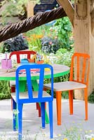 Bright coloured garden table in the summer house embellished with willow sculptures by Tom Hare - It's All About Community Garden - RHS Hampton Court Palace Flower Show 2017 -Designers: Andrew Fisher Tomlin and Dan Bowyer.