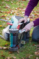 Using a brush to clean dirt and grass off mower blades before winter, November