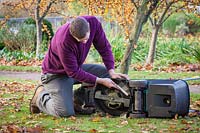 Using a brush to clean dirt and grass off mower blades before winter