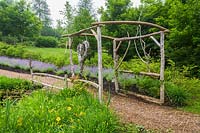 Rustic wooden arbour and mulch footpath edged with Hemerocallis 'Stella de Oro' and Nepeta in early summer. Le Jardin de Francois garden, Quebec, Canada. 