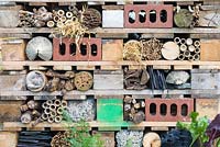A bug hotel built from wood offcuts, palettes, leftover bricks, bamboo lengths, branches, straw and pipes. 