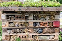 A bug hotel built from wood offcuts, leftover bricks, bamboo lengths, branches, straw and pipes.