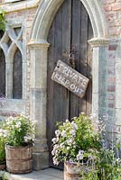A Gothic entrance flanked by recycled wooden barrels planted with roses.