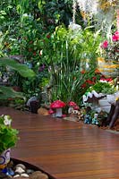 Detail of a curved timber walkway with shade loving plants and a collection of toys, pots and garden ornaments featuring a group red and white fairy toadstools.