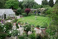 Overview of garden with greenhouse and cold frames, neat stripy lawn, paved terrace with pots and Lutyens bench, oak pergola. Planting includes Cotinus coggyria, Rosa 'Dublin Bay' ,Rosa 'Crocus', Rosa 'Iceberg', Rosa 'Phyllis Bide', Rosa 'Long John Silver' .