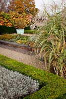 Miscanthus sinensis 'Variegatus' planted by Buxus - Box - low hedge containing Lavender. Water Lily filled pond and Phormium tenax purpureum group planted in old copper tub backed with Vitis coignetiae.