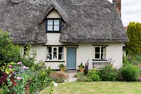 Caynton Cottage, a seventeenth century thatched cottage, overlooks a lawn edged in perennials.