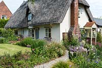 Caynton Cottage, a seventeenth century thatched cottage, overlooks a lawn and paths edged in perennials.