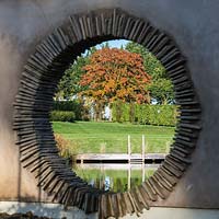 View through moongate to deck of natural swimming pool with autumn foliage of a copper sycamore.